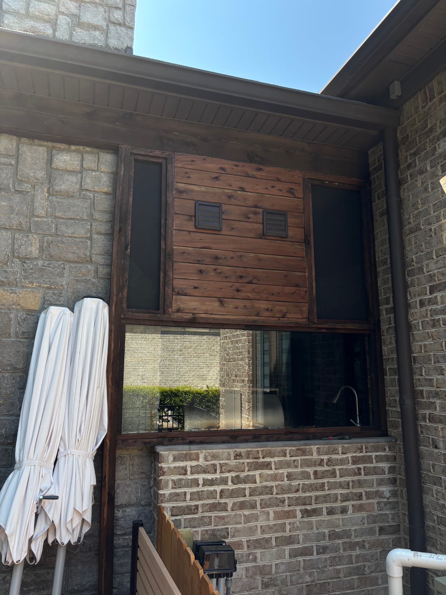 Stained cedar pass-through window surround with shutter panel and screened openings on a brick home