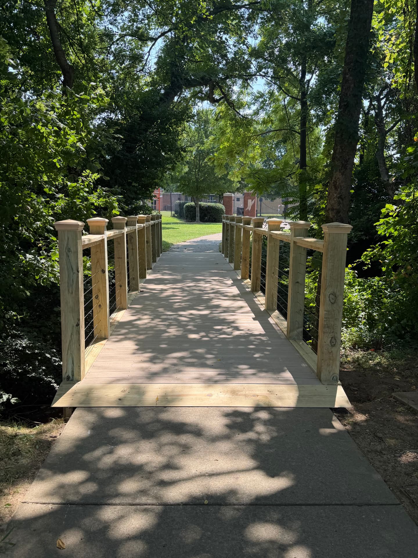 Custom pressure-treated footbridge with cable railing over a creek on a wooded trail